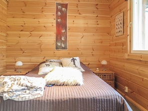 Quarto de cabana de madeira com cama, almofadas, manta e quadro na parede.