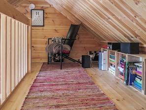 Quarto de sótão com teto inclinado, uma cadeira preta, tapete estampado e estantes cheias de livros.