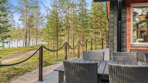 Ett trädäck med möbler i rotting, ett avspärrningsrep och utsikt över en skog och en sjö.