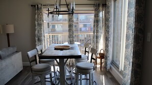 A dining area with a table, chairs, and a chandelier. There is a balcony with a railing and a view of buildings. - Spectacular Ocean View from Patio! (Rehoboth Beach)