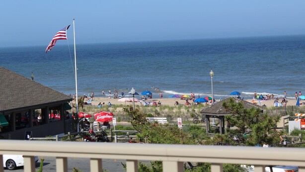 A beach scene with a flag, umbrellas, and people. - Spectacular Ocean View from Patio! (Rehoboth Beach)