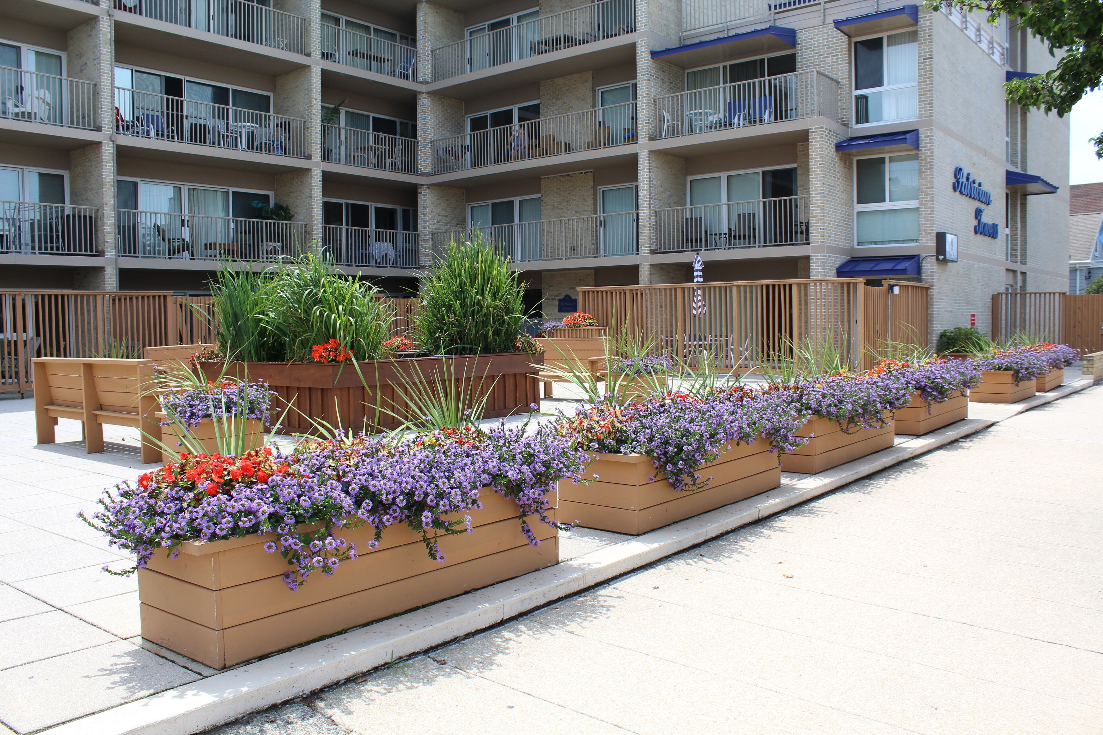 A multi-story hotel with balconies, outdoor seating, and flower planters along the walkway.