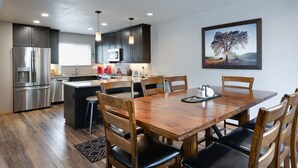 A modern kitchen with dark cabinets, stainless steel appliances, and a wooden dining table with chairs. - Blue Granite Off Main Townhome: Updated, Great Location (Frisco)