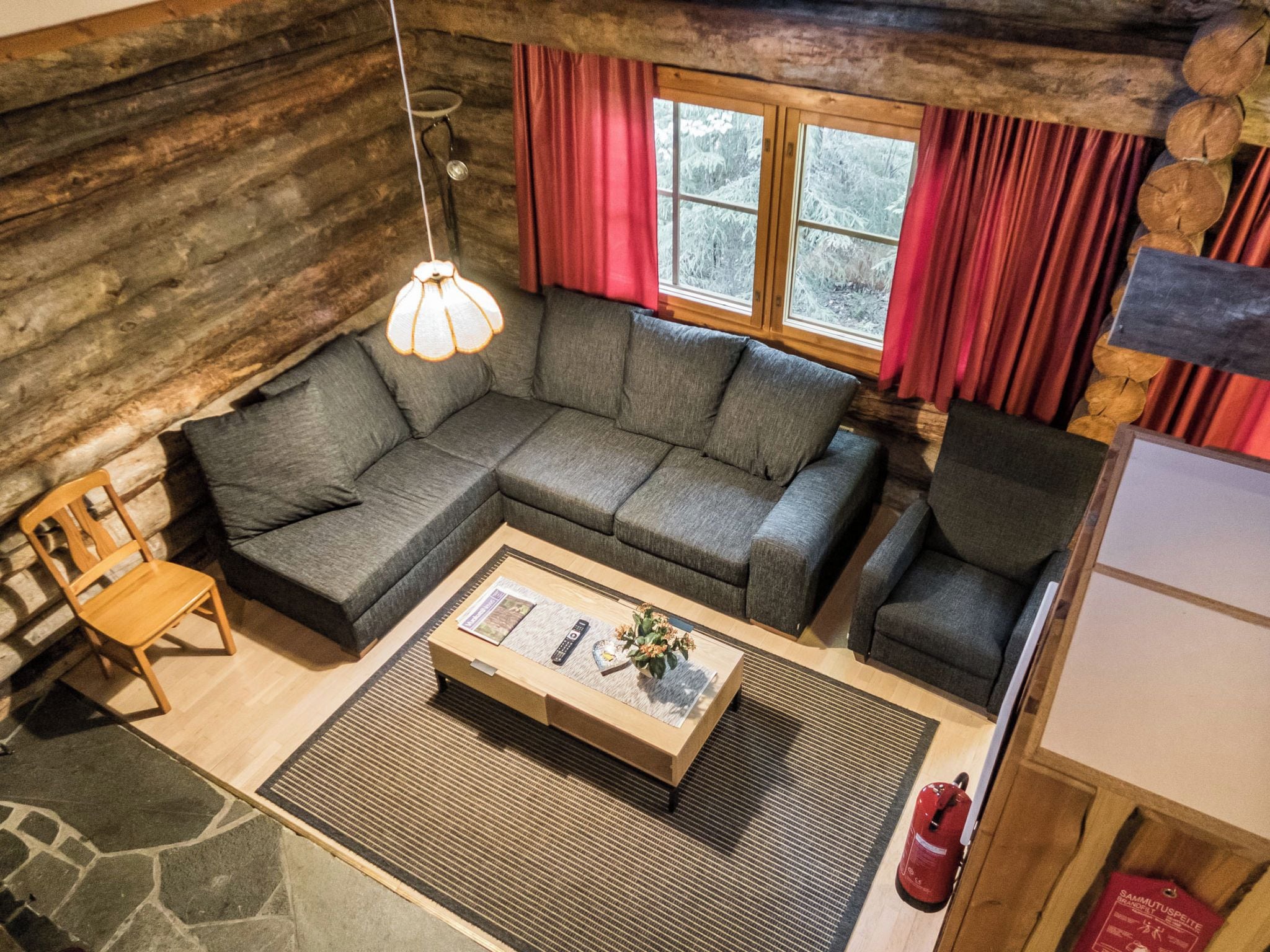 Un intérieur de chalet chaleureux avec un canapé d’angle, une table basse en bois, un fauteuil et une fenêtre avec des rideaux.