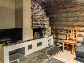 L’intérieur d’une cabane en rondins, avec une cheminée en pierre, un téléviseur posé sur une étagère en pierre et une chaise en bois.