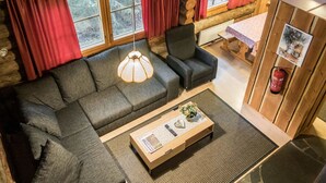 L’intérieur d’une cabane en rondins, avec un canapé, un fauteuil et une table basse sur laquelle repose un journal.