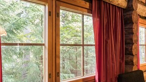 Une chambre de style rustique, avec de grandes fenêtres, un rideau rouge et un canapé gris.