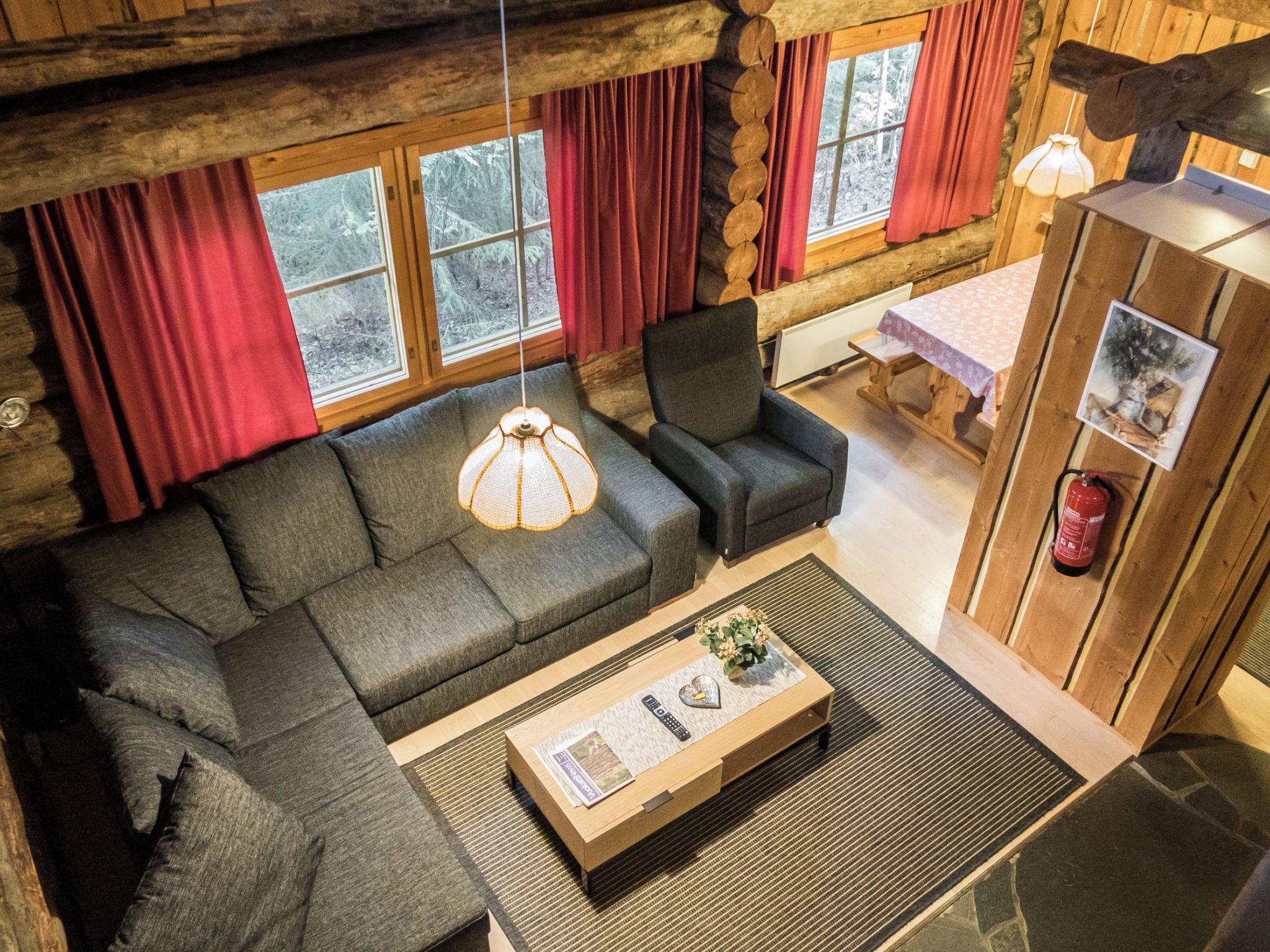 L'intérieur d'un chalet en bois présente un canapé, un fauteuil et une table sur laquelle se trouvent une télécommande et un objet en forme de cœur.