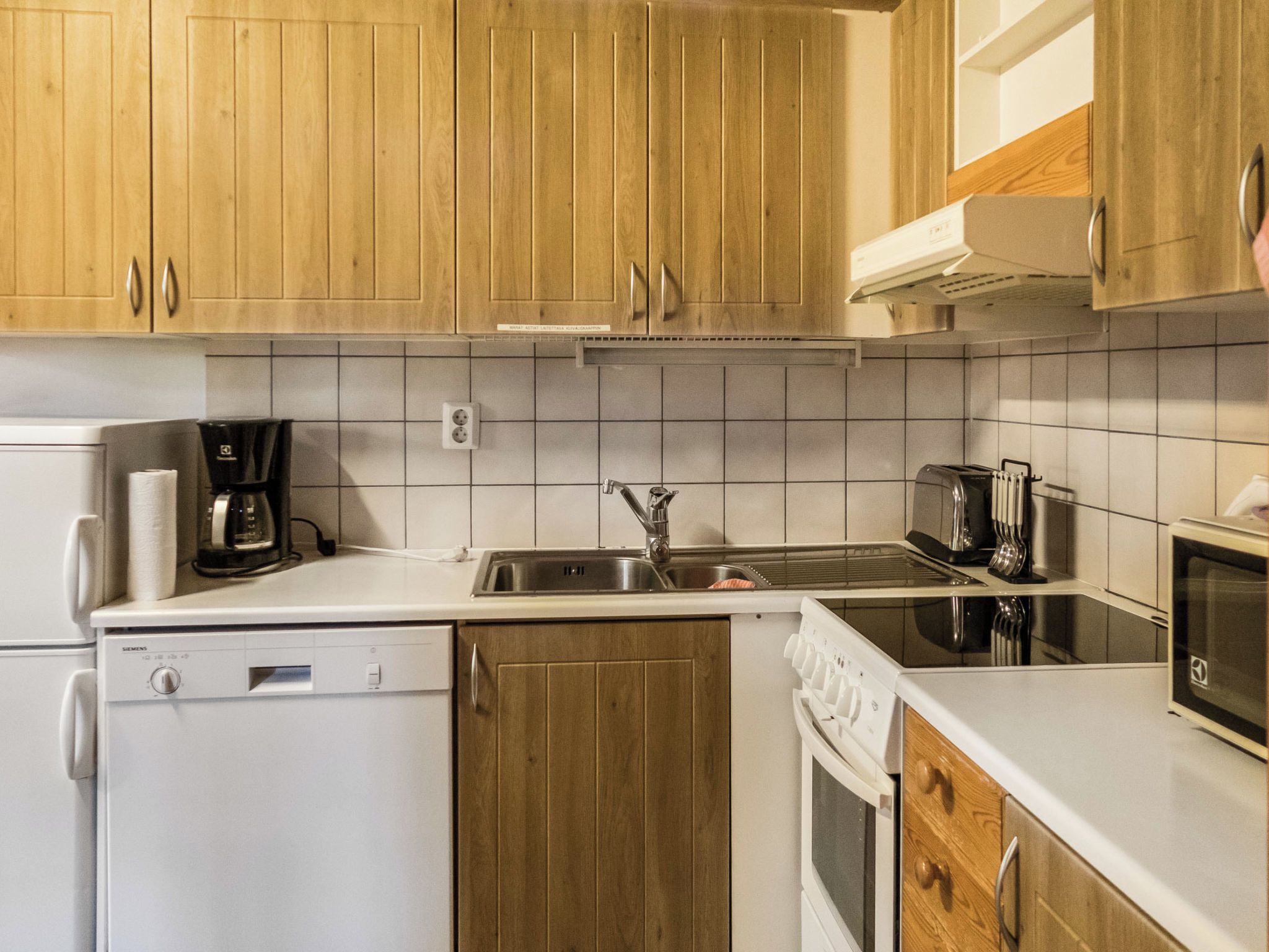 Une cuisine avec des meubles de rangement en bois, un lave-vaisselle, une machine à café, un grille-pain, un four à micro-ondes et une cuisinière.