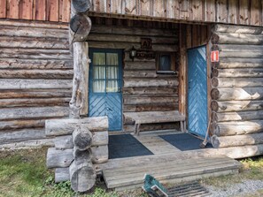 A rustic log cabin with a blue door, a small bench outside, and a wooden staircase leading up to the entrance.