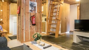 Un intérieur rustique avec des poutres en bois, une échelle en bois, un extincteur, un téléviseur et une télécommande posée sur une table.