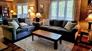 Ein gemütliches Wohnzimmer mit einem Ecksofa, zwei Nachttischen mit Lampen, einem Couchtisch und einem Bücherregal.