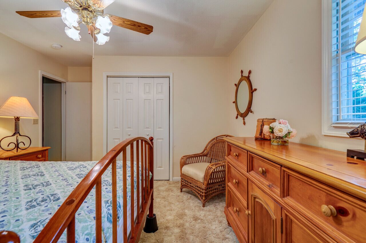 A bedroom with a wooden bed, a dresser, a wicker chair, a ceiling fan, and a window with blinds.