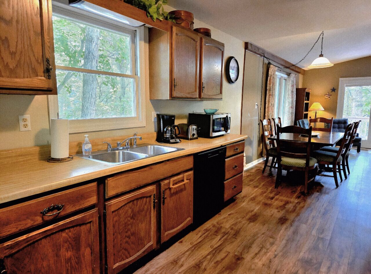 A kitchen with wooden cabinets, a sink, a dishwasher, a microwave, and a dining area with a table and chairs.