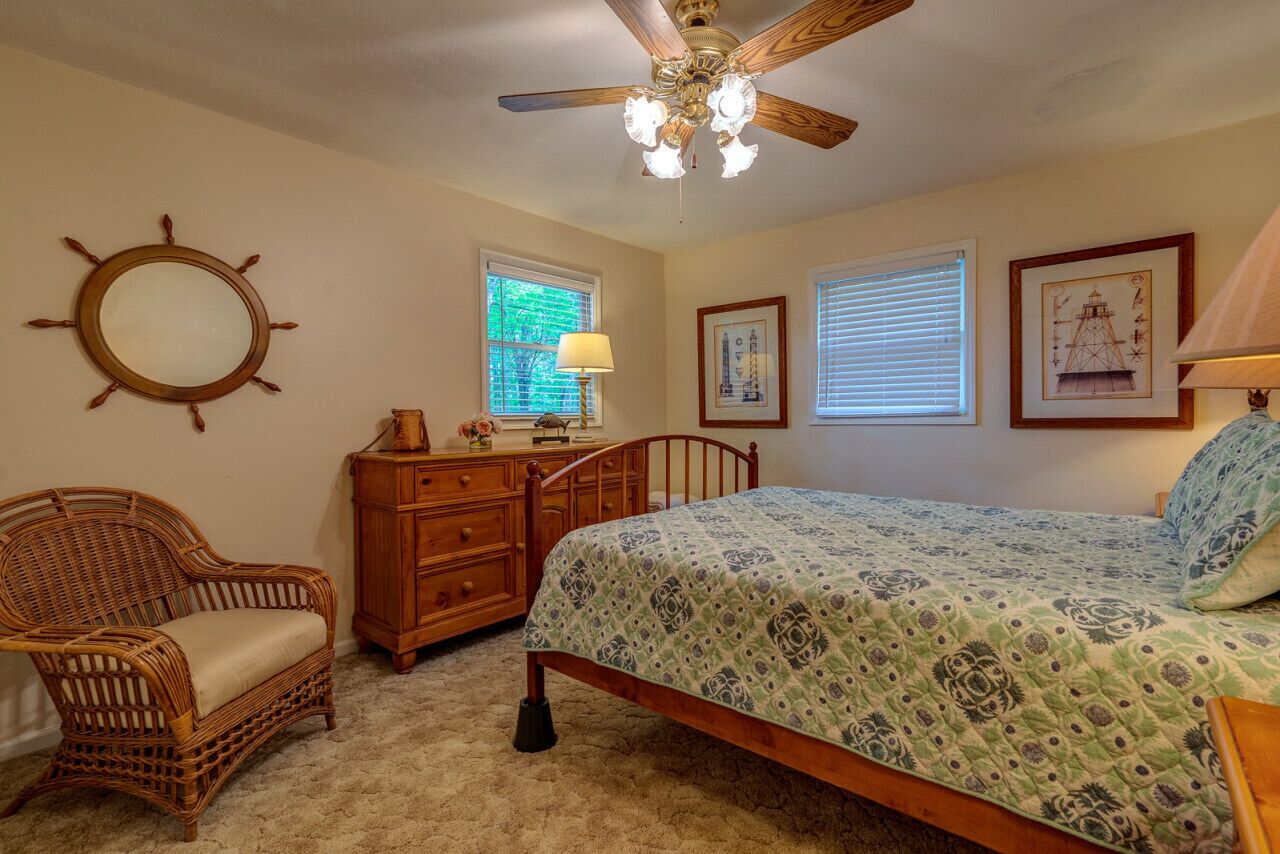A bedroom with a bed, a chair, a dresser, a ceiling fan, and a wall-mounted mirror.