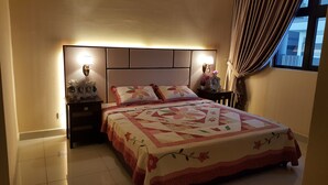Een net opgemaakt bed met een bloemenquilt, twee bedlampen en een nachtkastje met een ingelijste foto en decoratieve objecten.