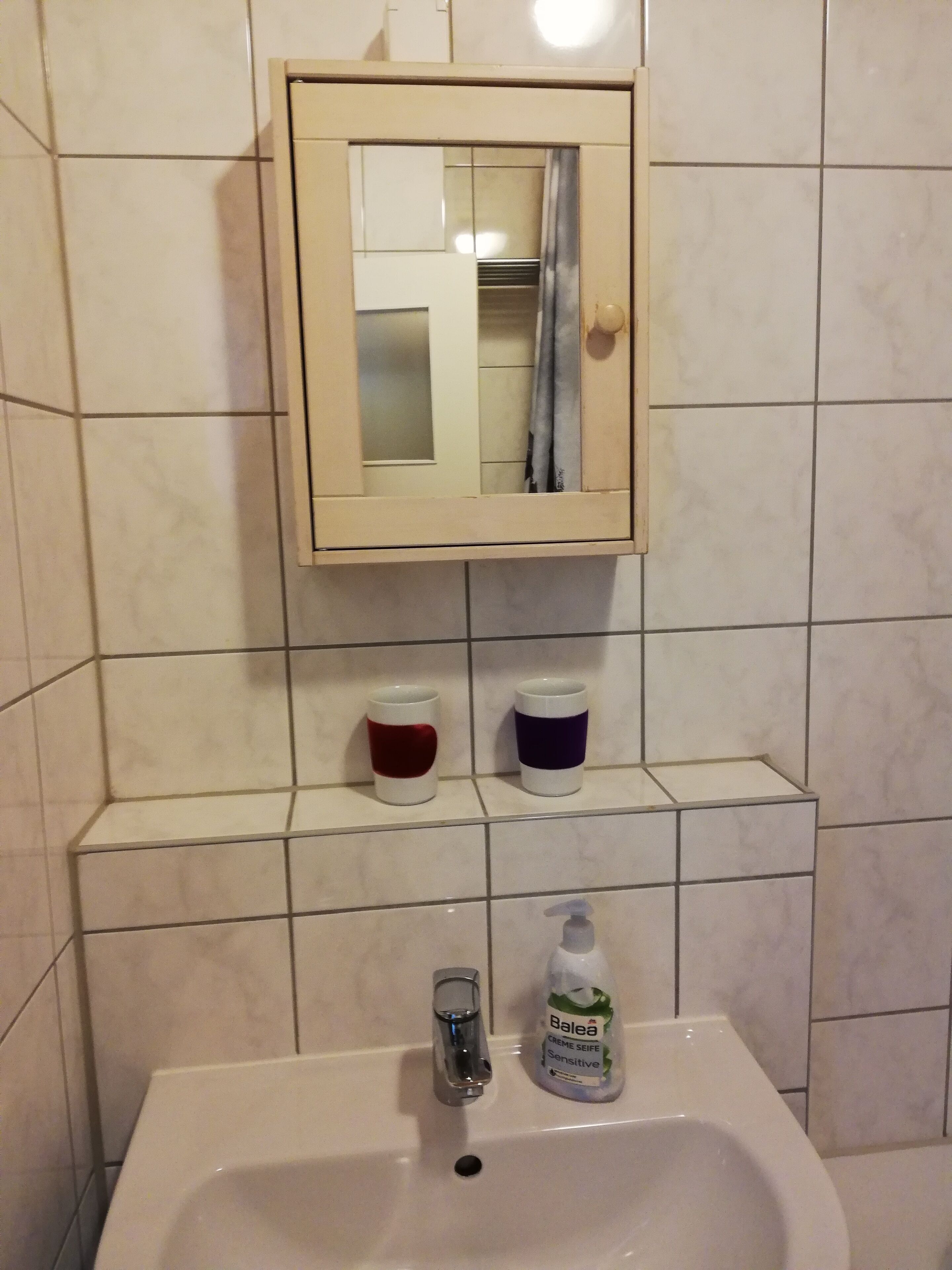 A bathroom with a sink, a mirror, and two cups on a shelf.