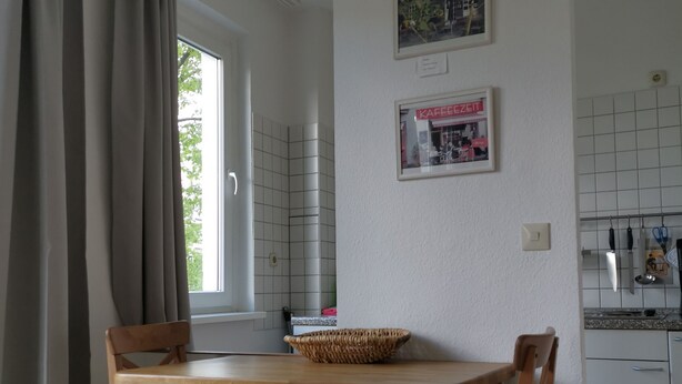 A small kitchen with two wooden chairs, a table, and a window with curtains. - We invite you to our apartment (Bezirk Charlottenburg-Wilmersdorf)