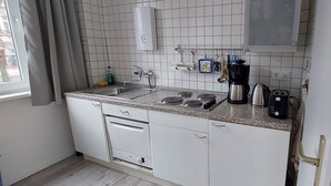 A compact kitchen with white cabinets, a stainless steel sink, a gas stove, a coffee maker, and a toaster. - We invite you to our apartment (Bezirk Charlottenburg-Wilmersdorf)