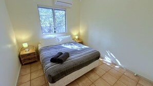 Une chambre à coucher comprenant un lit, deux lampes de chevet, une fenêtre et un climatiseur fixé au mur.