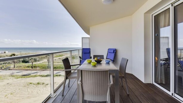 Een balkon met een tafel en stoelen, met uitzicht op een strand.