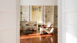 Un salon spacieux doté d’un parquet en bois, d’un canapé blanc, d’une table basse et d’une bibliothèque remplie de livres et d’objets décoratifs.