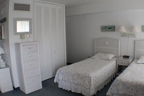 A bedroom with two single beds, a dresser, a nightstand, and a wall-mounted lamp. - Efficiency with tropical coastal decor! (Rehoboth Beach)