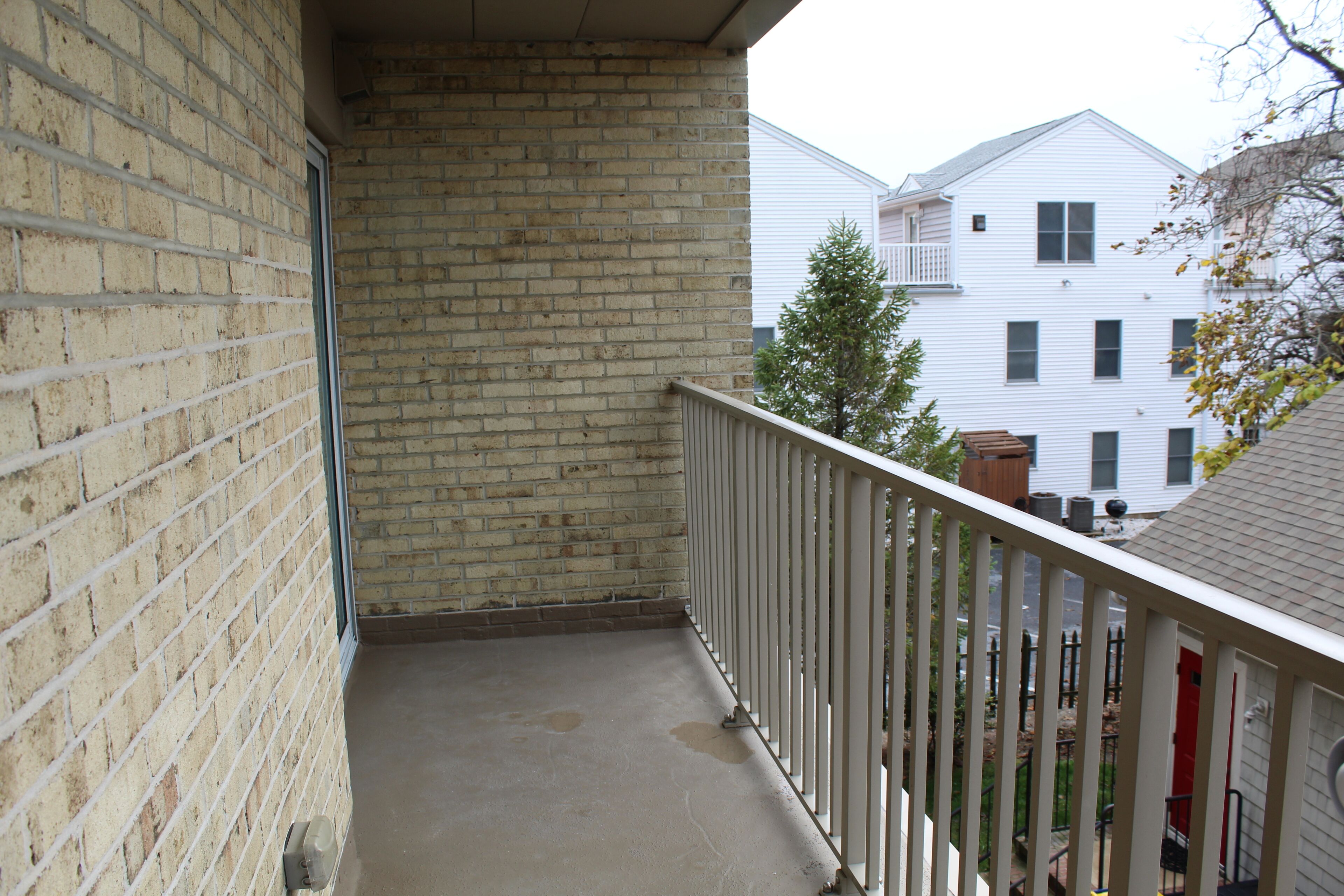 Ein schmaler Balkon, an einer Seite eine Ziegelwand, an der anderen eine weiße Brüstung.