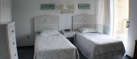 Une chambre avec deux lits simples, une table de chevet, une horloge murale et une fenêtre avec des rideaux.