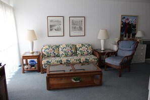 A living room with a floral sofa, a wooden coffee table, a blue armchair, and two framed pictures on the wall. - Efficiency with tropical coastal decor! (Rehoboth Beach)