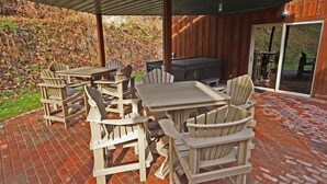 An outdoor patio with wooden Adirondack chairs and a table, a barbecue grill, and a glass door leading to a covered area. - Hidden Valley - modern, rustic, unique (Rockbridge)