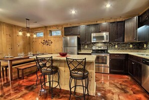 Una cocina con armarios de madera, electrodomésticos de acero inoxidable, una zona de comedor con una mesa y sillas, y un tazón rojo en la isla.