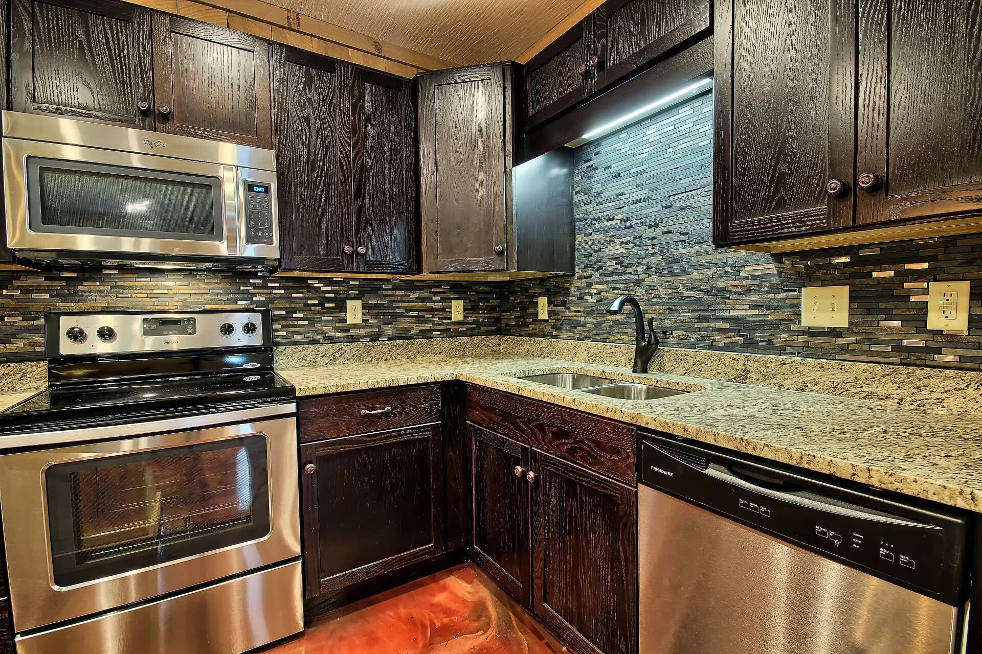 A kitchen with dark wood cabinets, a stainless steel microwave, oven, and dishwasher, and a granite countertop.