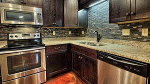 Una cocina con gabinetes de madera oscura, un microondas, horno y lavavajillas de acero inoxidable, y una encimera de granito.