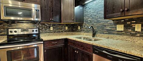 A kitchen with dark wood cabinets, a stainless steel microwave, oven, and dishwasher, and a granite countertop.