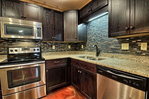 A kitchen with dark wood cabinets, a stainless steel microwave, oven, and dishwasher, and a granite countertop. - Hidden Valley - modern, rustic, unique (Rockbridge)