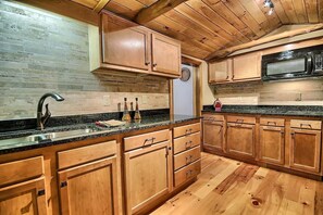 Une cuisine avec des meubles en bois, un plan de travail en granit et un micro-ondes noir.