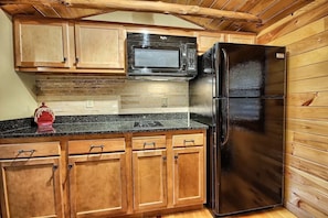 Una cocina con armarios de madera, un refrigerador negro y un microondas.