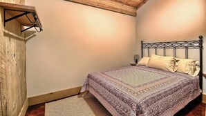A bedroom with a wooden ceiling, a bed with a patterned bedspread, a bedside table, and a wall-mounted shelf. - Hidden Valley - modern, rustic, unique (Rockbridge)