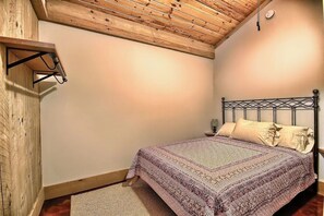 Une chambre avec un plafond en bois, un lit recouvert d’une couvre-lit à motifs, une table de chevet et une étagère fixée au mur.