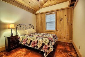 A bedroom with a wooden ceiling, a bed with a floral bedspread, a nightstand with a lamp, and a window with blinds. - Hidden Valley - modern, rustic, unique (Rockbridge)
