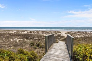 Une promenade en bois qui mène à une plage bordée de dunes et dotée d’une végétation clairsemée.
