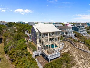 Une maison à plusieurs étages avec une piscine, entourée d’une plage de sable et d’une végétation luxuriante.