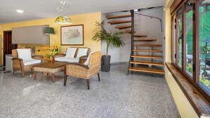 A spacious living area with wicker furniture, a staircase, and a view of greenery through large windows. - El Balcon by Interhome (Córdoba/Baena)