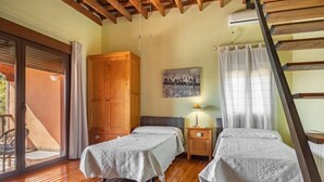 A room with two beds, wooden flooring, a large wardrobe, a painting on the wall, and a staircase. - El Balcon by Interhome (Córdoba/Baena)