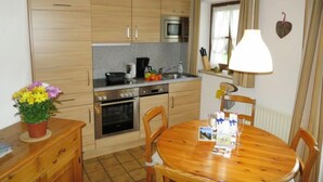 Une cuisine compacte avec des meubles en bois, un four à micro-ondes, une cuisinière et un évier. On y trouve une table à manger avec des chaises et une petite plante en pot.