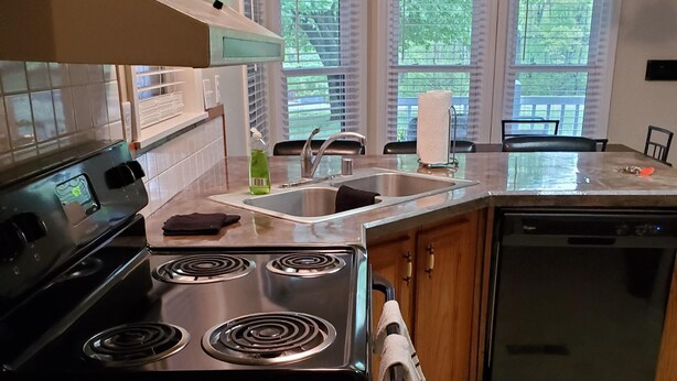 A kitchen with a stove, sink, and dishwasher. There are windows with blinds, a chandelier, and a tiled floor. - Fisherman, Traveling Workers and Vactioners love the Barefoot Retreat (Eddyville)