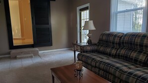 A living room with a plaid sofa, a wooden coffee table, a lamp, and a window with blinds. - Fisherman, Traveling Workers and Vactioners love the Barefoot Retreat (Eddyville)