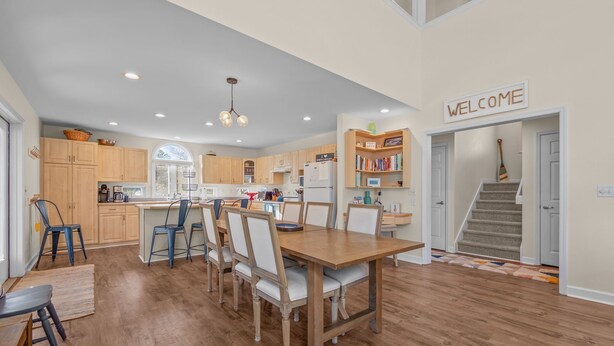 A modern kitchen with wooden cabinets, a dining area with a wooden table and chairs, and a staircase leading to a second floor.