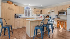A modern kitchen with wooden cabinets, a central island with bar stools, a microwave, and a refrigerator.